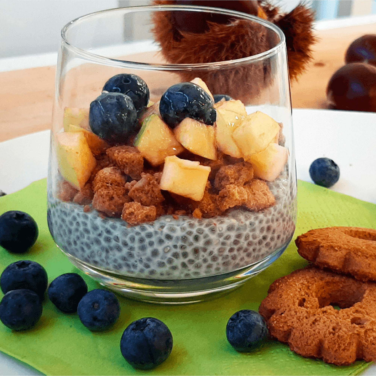 Bicchiere con pudding di chia, biscotti sbriciolati, frutta a pezzi e mirtilli.