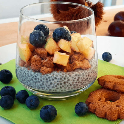 Bicchiere con pudding di chia, biscotti sbriciolati, frutta a pezzi e mirtilli.