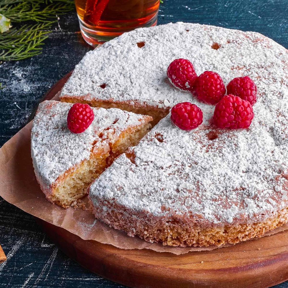 Torta di chufa con spolverata di zucchero a velo e guarnita con lamponi, con una fetta tagliata.