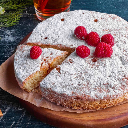 Torta di chufa con spolverata di zucchero a velo e guarnita con lamponi, con una fetta tagliata.