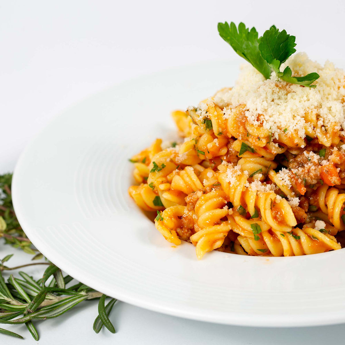 Fusilli con funghi in granuli, guarnizione grattugiata e prezzemolo in un piatto bianco.