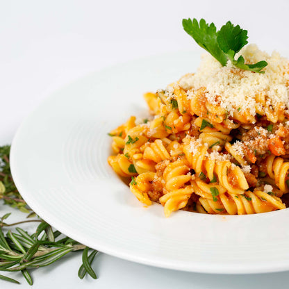 Fusilli con funghi in granuli, guarnizione grattugiata e prezzemolo in un piatto bianco.