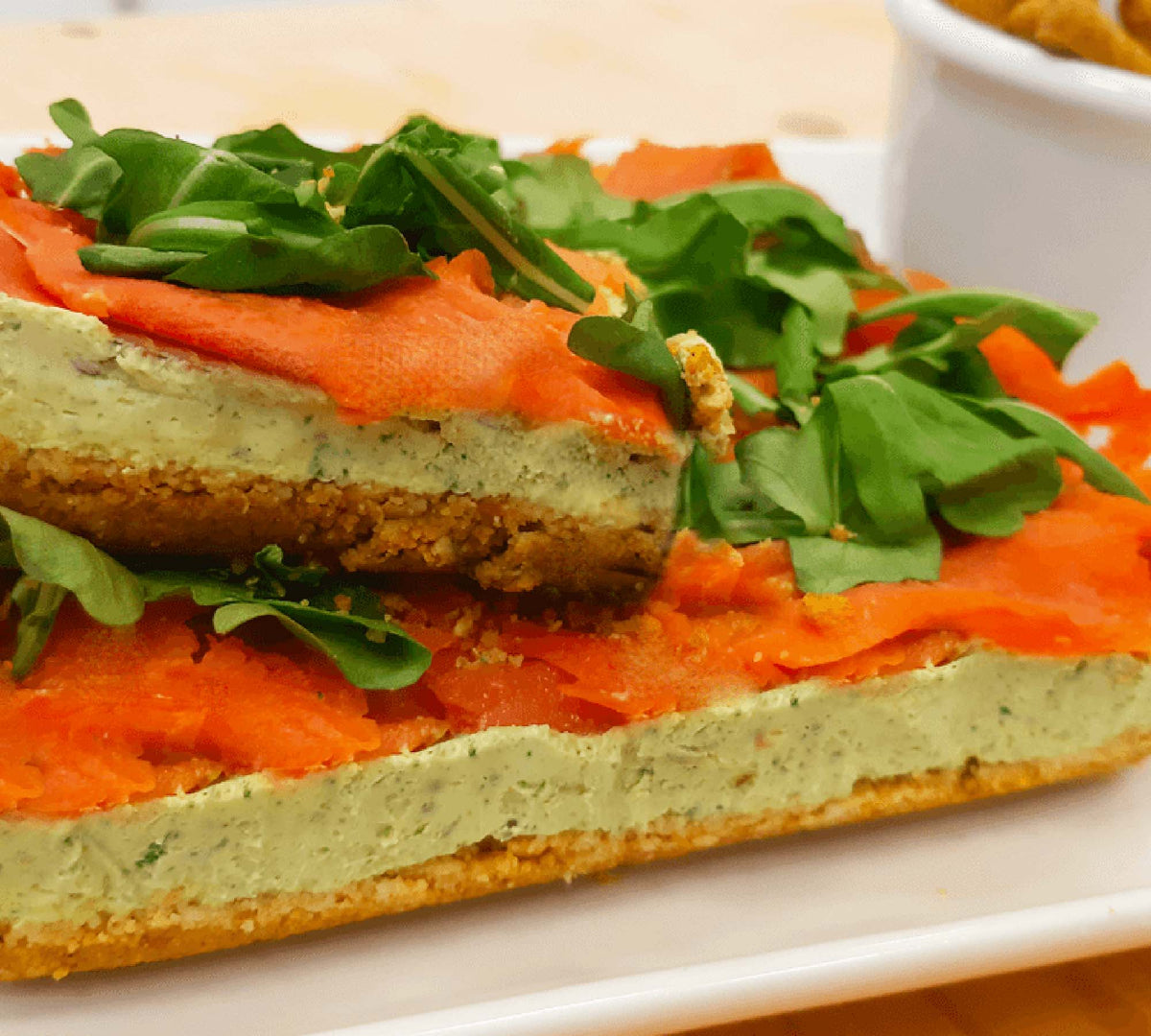 Preparazione salata a strati con base croccante di grissini, crema verde, salmone e rucola.